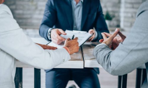 Couple sitting at desk in the bank and signing loan agreement. Shot of three business persons filling in paperwork in an office. Business persons signing a document in board room.